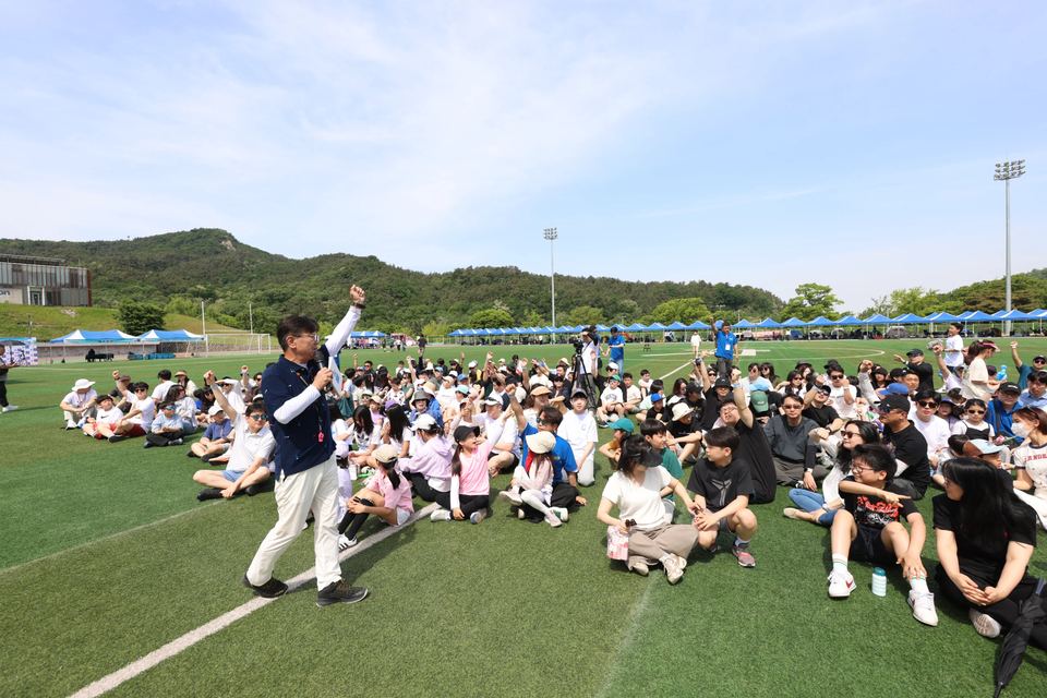 운동장에서 앉은 참가자들 앞에서 진행하는 장면 · 체육 행사