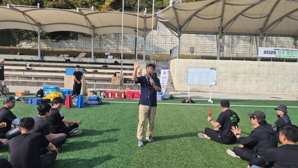 야외 체육 행사에서 진행자가 참가자들에게 손을 든 장면 · 체육 행사