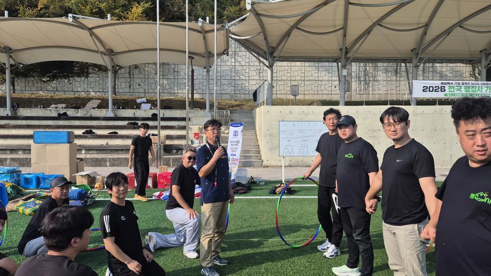 잔디 운동장에서 참가자들이 둘러서 진행을 듣는 장면 · 체육 행사
