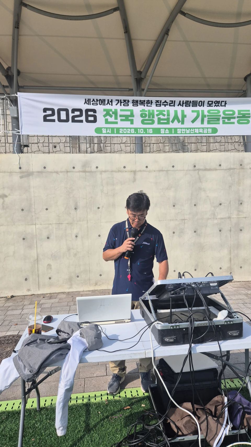 음향 장비 앞에서 마이크를 든 진행자와 현수막 · 체육 행사