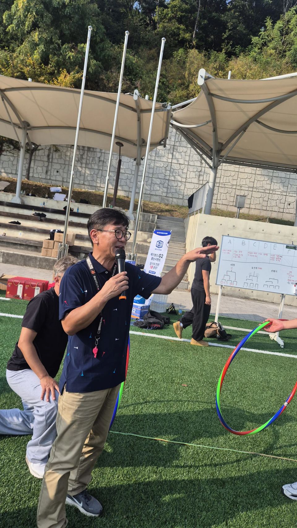 운동장에서 마이크를 들고 게임을 설명하는 진행자 · 체육 행사