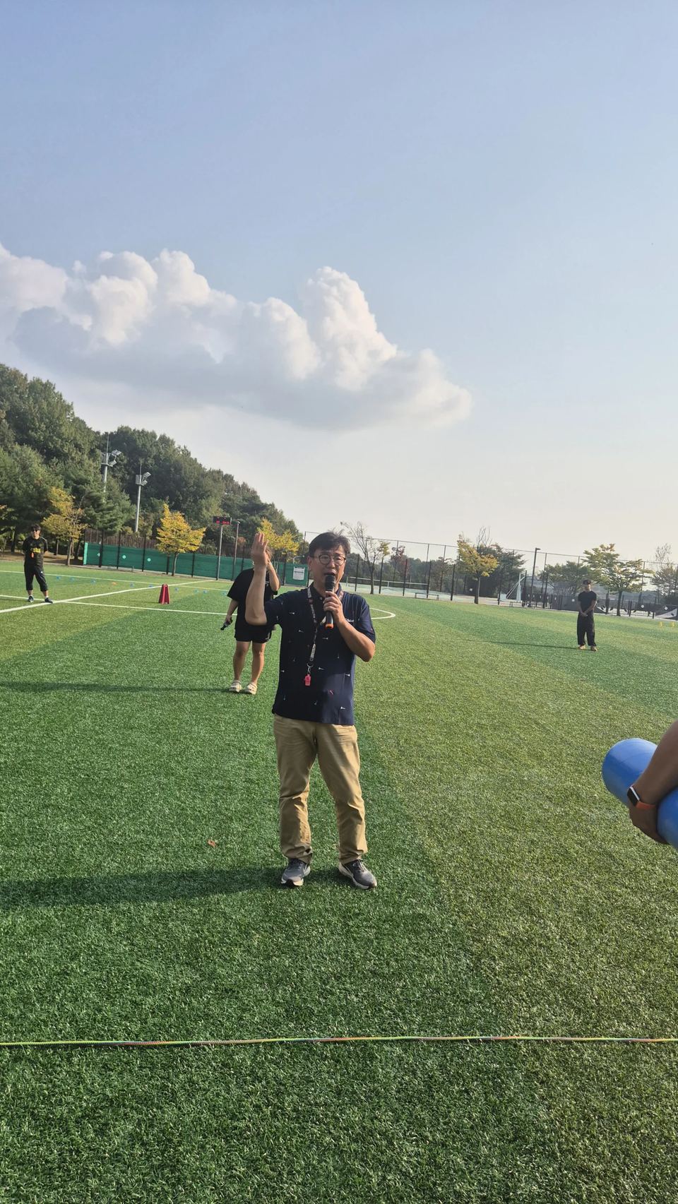 푸른 하늘 아래 운동장에서 마이크를 든 진행자 · 체육 행사